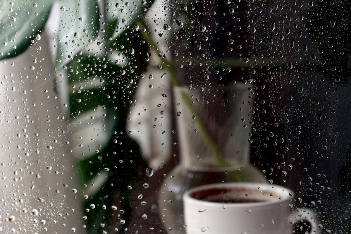 雨の窓辺に置かれたコーヒーとキャンドル
