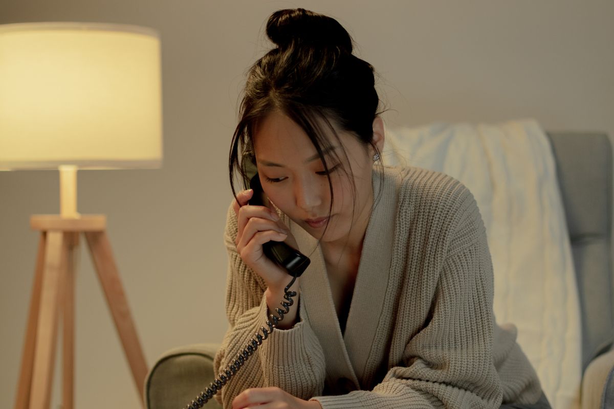 自宅であたたかい灯りの下、電話で話す女性